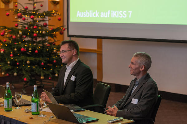 iKISS-Entwickler Bernhard Penski und Peter Cochius geben einen Ausblick auf iKISS 7, im Hintergrund ein Weihnachtsbaum und die Leinwand mit den Vortragsfolien