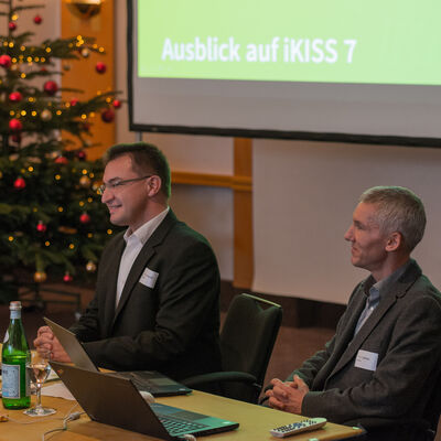 Bild vergrößern: iKISS-Entwickler Bernhard Penski und Peter Cochius geben einen Ausblick auf iKISS 7, im Hintergrund ein Weihnachtsbaum und die Leinwand mit den Vortragsfolien